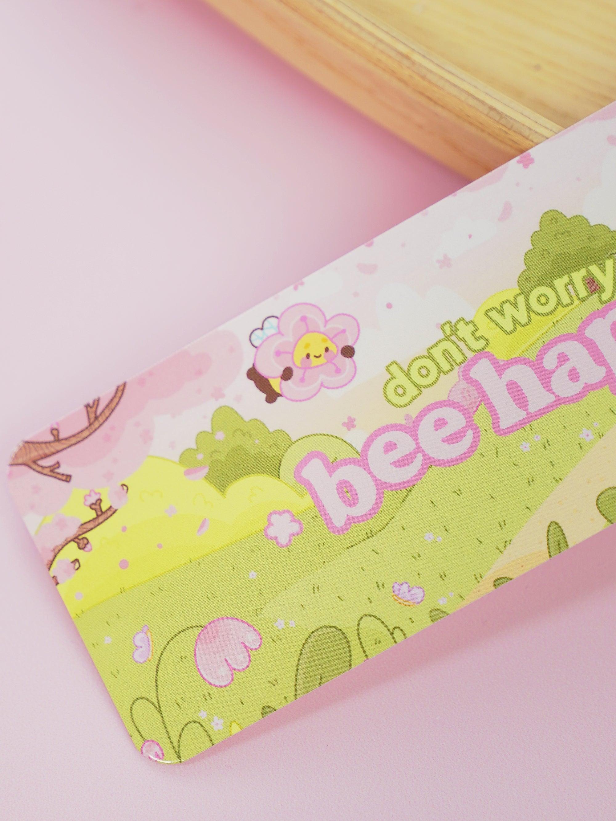 Image of Bumblebutt Bee bookmark featuring a bee resting on a pink cherry blossom flower. 2
