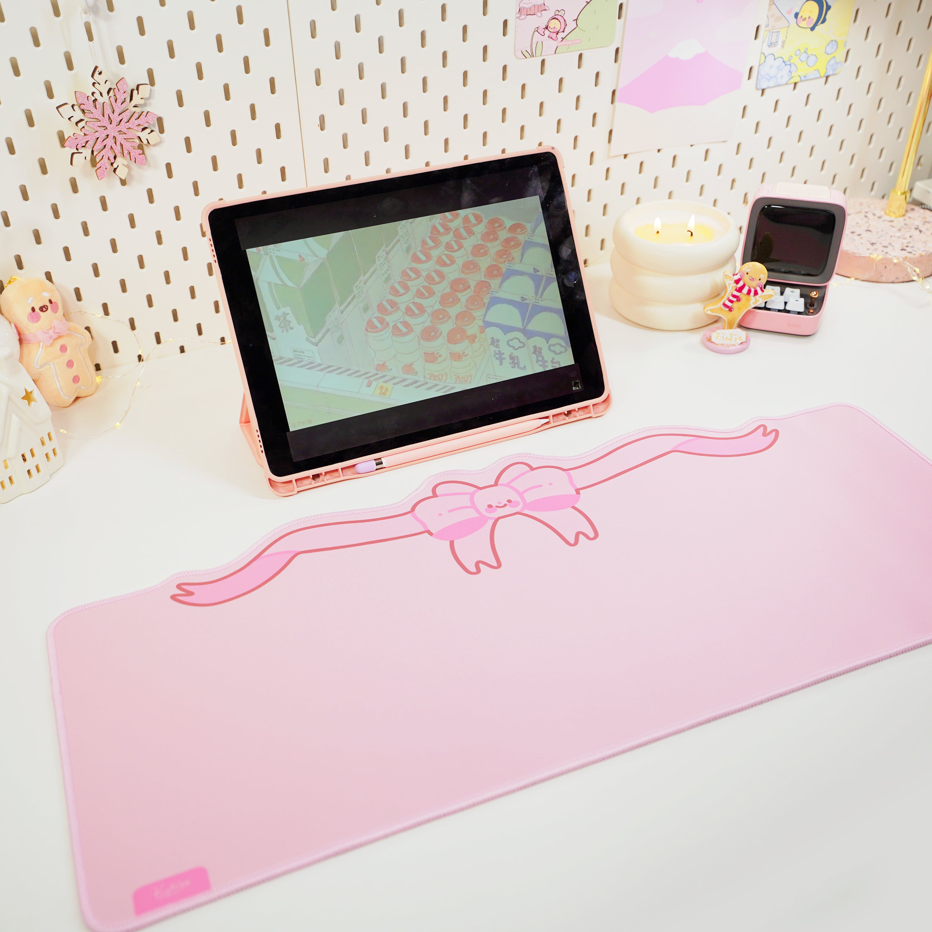 A large, pastel pink coquette bow gaming desk pad displayed on a desk with a laptop and smartphone.